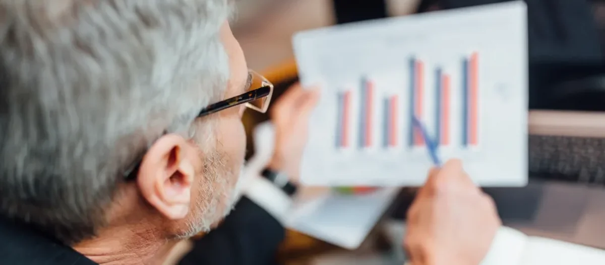 Analyst reviewing printed white paper documents with colored bar charts and analytical tables.